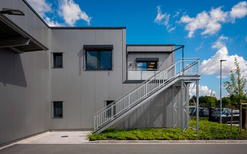 Architekturaufnahme einer Gewerbeimmobilie mit Metalltreppe auf die Sonnenterrasse bei sonnigem Wetter.